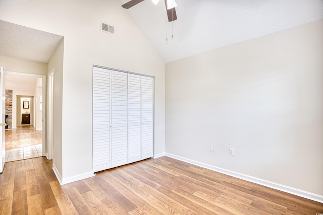 unfurnished bedroom with light hardwood / wood-style flooring, ceiling fan, high vaulted ceiling, a fireplace, and a closet