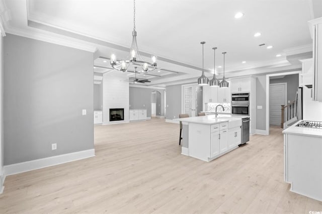 kitchen featuring a large fireplace, a kitchen island with sink, light hardwood / wood-style flooring, white cabinetry, and hanging light fixtures