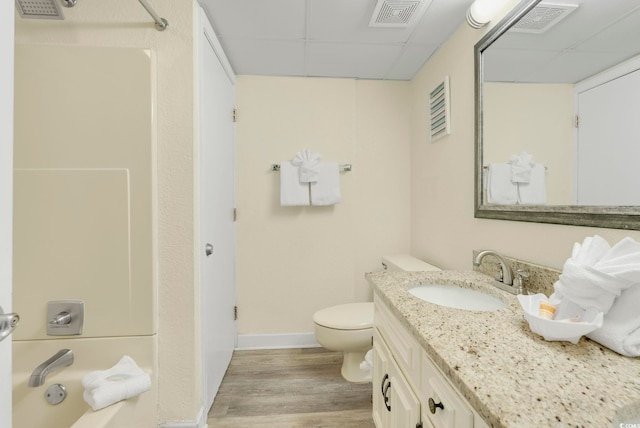 full bathroom featuring toilet,  shower combination, wood-type flooring, vanity, and a drop ceiling