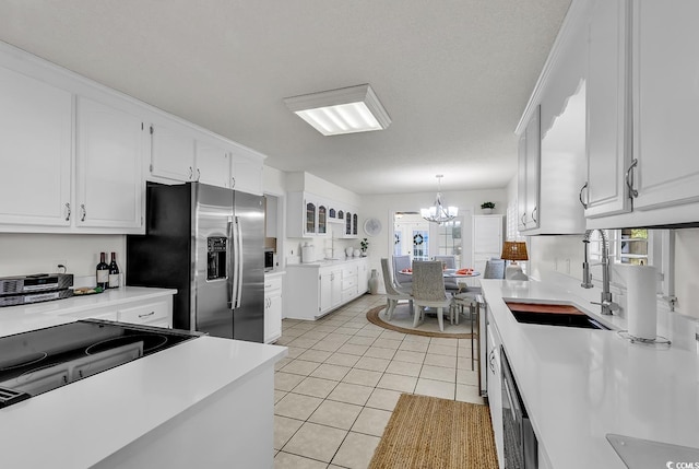 kitchen with stainless steel appliances, sink, light tile patterned floors, a chandelier, and white cabinetry