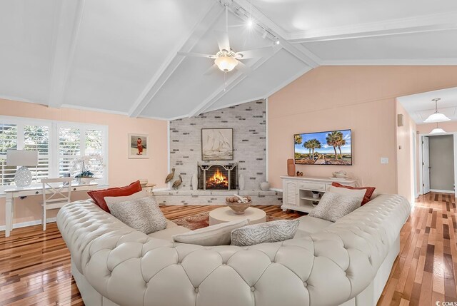 living room with ceiling fan, rail lighting, a brick fireplace, lofted ceiling, and light wood-type flooring