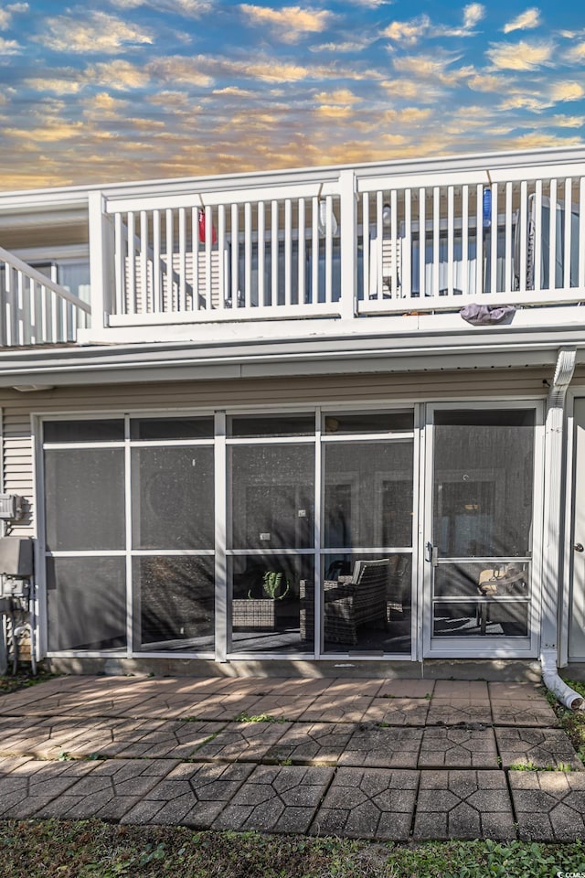 back house at dusk featuring a sunroom, a balcony, and a patio