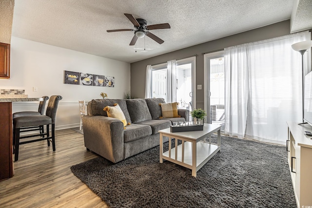 living room with a textured ceiling, ceiling fan, and dark wood-type flooring