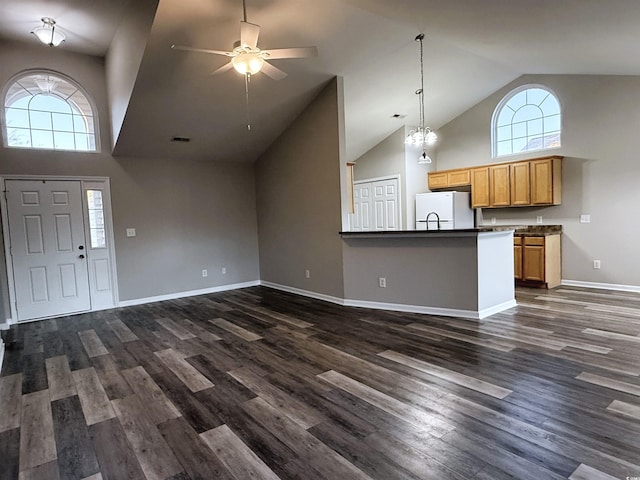 interior space featuring ceiling fan with notable chandelier, a healthy amount of sunlight, dark wood-type flooring, and high vaulted ceiling