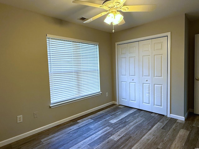 unfurnished bedroom featuring ceiling fan, multiple windows, dark wood-type flooring, and a closet