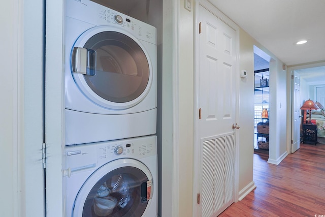 clothes washing area featuring hardwood / wood-style floors and stacked washer / drying machine