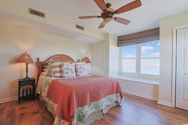 bedroom with a textured ceiling, ceiling fan, a water view, and dark wood-type flooring