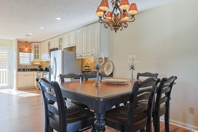 dining area with sink, light hardwood / wood-style flooring, a textured ceiling, and an inviting chandelier