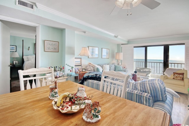 dining room with wood-type flooring, a water view, ceiling fan, and crown molding