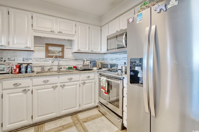 kitchen featuring sink, stainless steel appliances, light tile patterned floors, decorative backsplash, and white cabinets