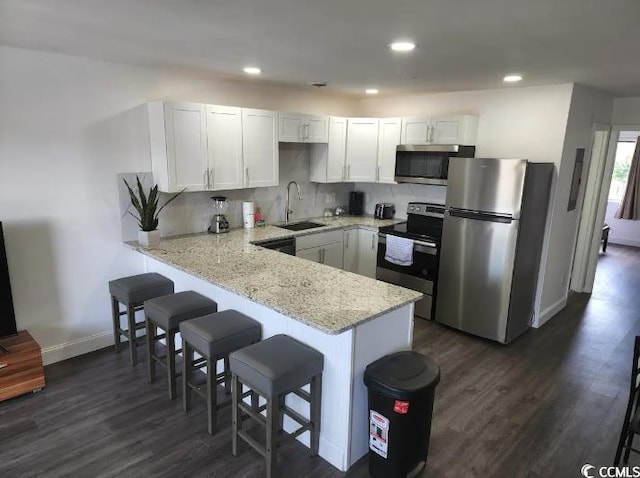 kitchen featuring appliances with stainless steel finishes, white cabinetry, sink, kitchen peninsula, and light stone countertops