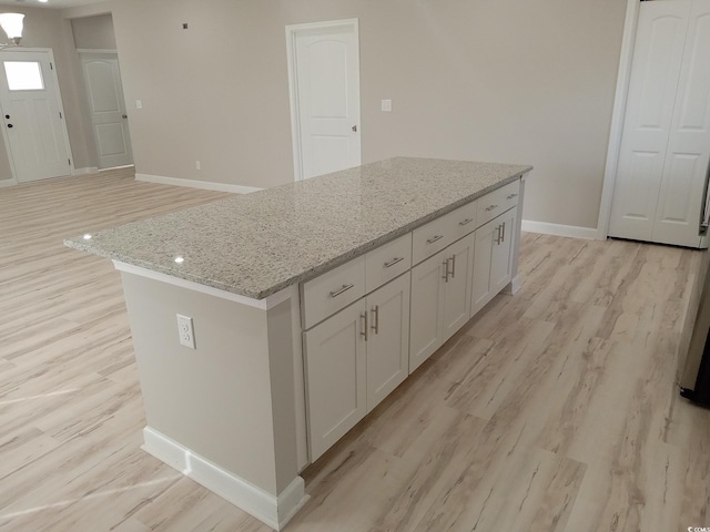 kitchen with baseboards, light wood-style flooring, a kitchen island, light stone counters, and white cabinetry