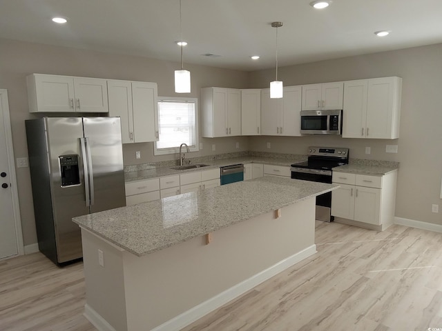 kitchen with light stone counters, a center island, stainless steel appliances, white cabinetry, and a sink