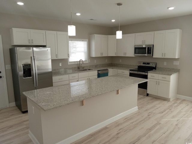 kitchen featuring a kitchen island, a sink, appliances with stainless steel finishes, white cabinetry, and decorative light fixtures