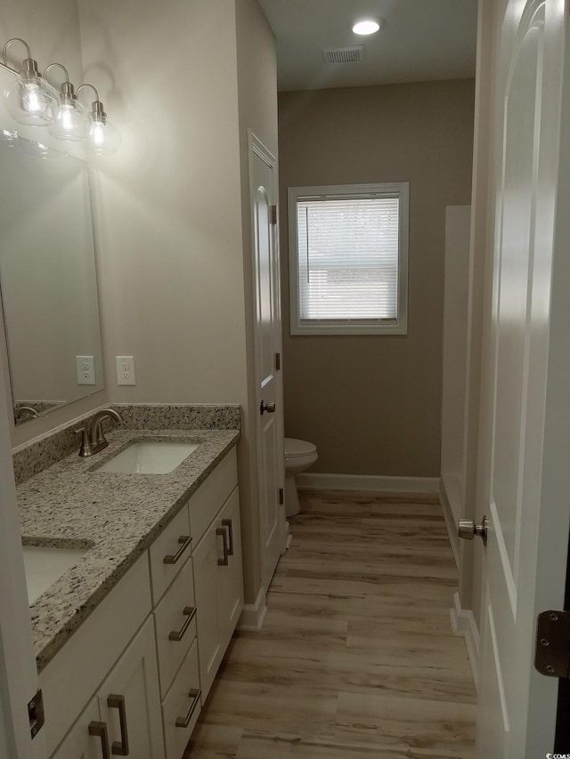 full bathroom with double vanity, visible vents, toilet, a sink, and wood finished floors