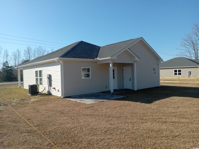 view of front of home featuring central air condition unit, a shingled roof, a front yard, and a patio