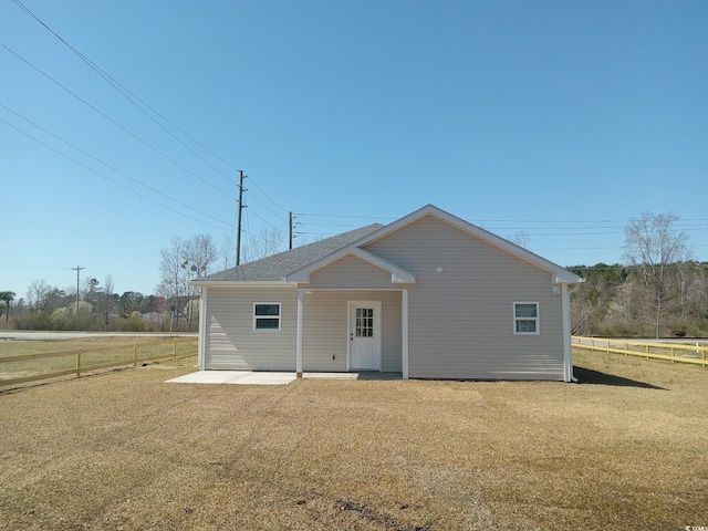 back of property with a shingled roof, a yard, and fence