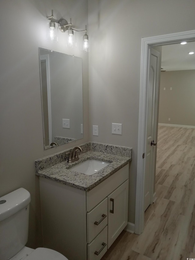 half bath featuring toilet, baseboards, wood finished floors, and vanity