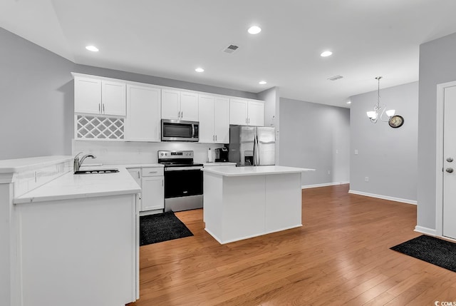 kitchen with pendant lighting, stainless steel appliances, kitchen peninsula, a notable chandelier, and light wood-type flooring