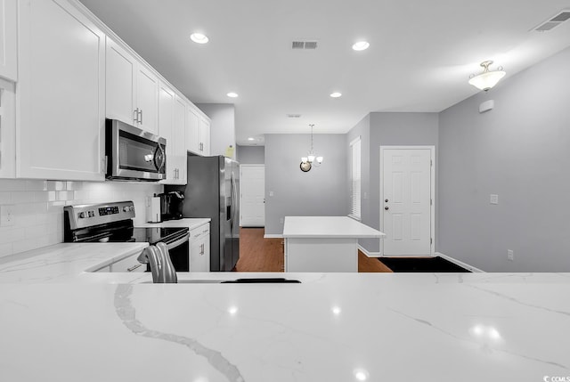 kitchen featuring light stone countertops, appliances with stainless steel finishes, white cabinetry, tasteful backsplash, and hanging light fixtures