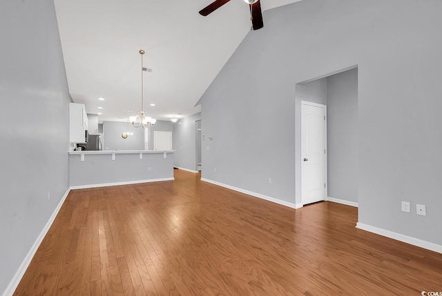 unfurnished living room with vaulted ceiling, ceiling fan with notable chandelier, and hardwood / wood-style flooring