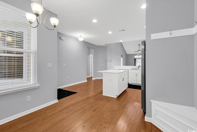 kitchen with vaulted ceiling, a notable chandelier, pendant lighting, a center island, and white cabinets