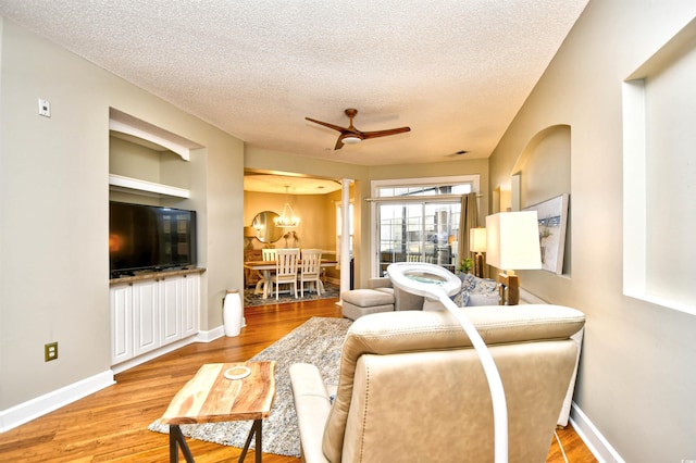 living room with wood-type flooring, ceiling fan with notable chandelier, and a textured ceiling