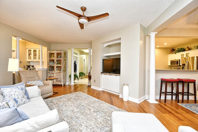 living room featuring ceiling fan, built in features, a textured ceiling, and light wood-type flooring