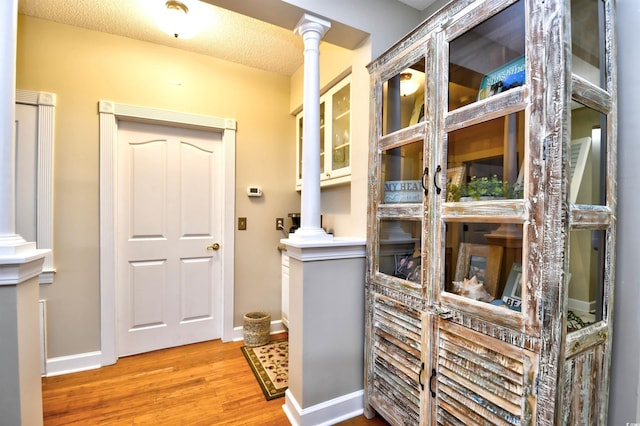 doorway featuring a textured ceiling, light hardwood / wood-style floors, and ornate columns