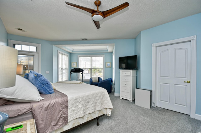 carpeted bedroom featuring a tray ceiling, ceiling fan, and a textured ceiling