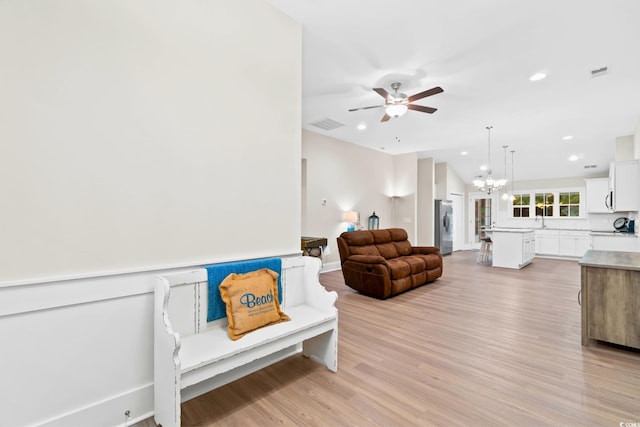 living room featuring ceiling fan with notable chandelier, sink, and light hardwood / wood-style flooring