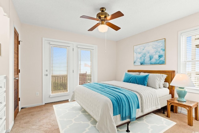 bedroom featuring access to exterior, multiple windows, light colored carpet, and ceiling fan