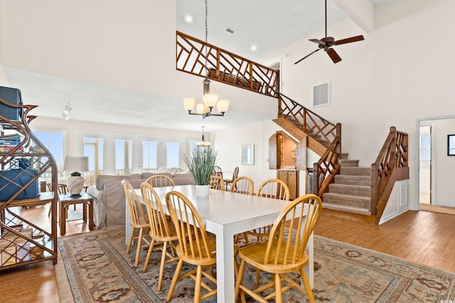 dining area featuring beamed ceiling, ceiling fan with notable chandelier, wood-type flooring, and a high ceiling