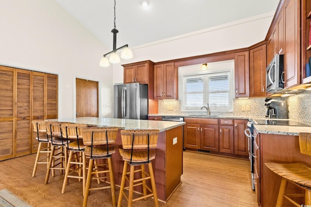 kitchen featuring appliances with stainless steel finishes, backsplash, a center island, hanging light fixtures, and a breakfast bar area