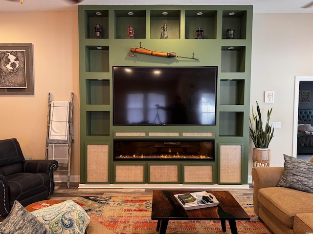 living area featuring built in shelves, a glass covered fireplace, and wood finished floors