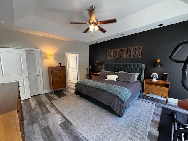 bedroom with a tray ceiling, dark wood-type flooring, a ceiling fan, and baseboards