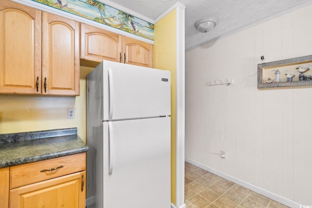 kitchen featuring a textured ceiling, white refrigerator, wooden walls, and light brown cabinets