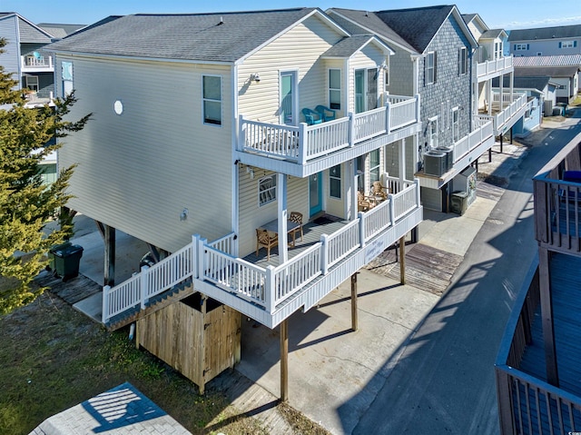 back of house featuring a shingled roof, a balcony, a residential view, and central air condition unit