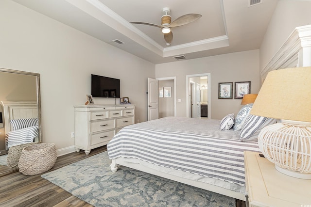 bedroom featuring connected bathroom, ceiling fan, a raised ceiling, hardwood / wood-style flooring, and ornamental molding