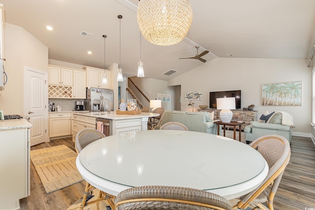 dining space featuring ceiling fan with notable chandelier, hardwood / wood-style flooring, vaulted ceiling, and sink