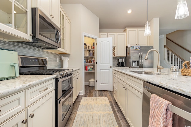 kitchen with backsplash, stainless steel appliances, sink, pendant lighting, and hardwood / wood-style flooring