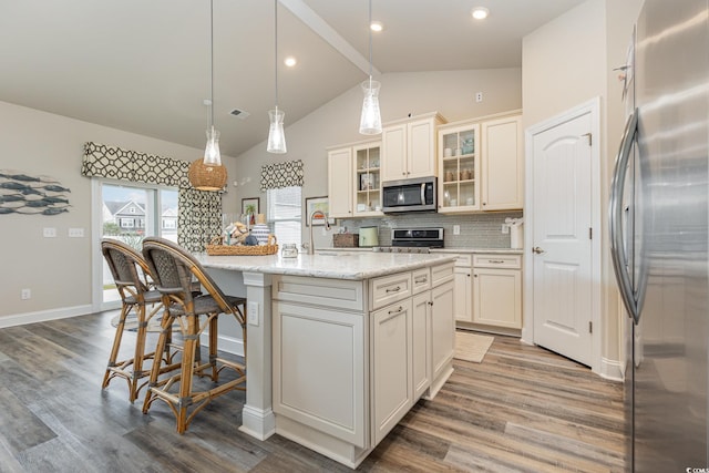 kitchen with lofted ceiling, a kitchen island with sink, appliances with stainless steel finishes, and tasteful backsplash