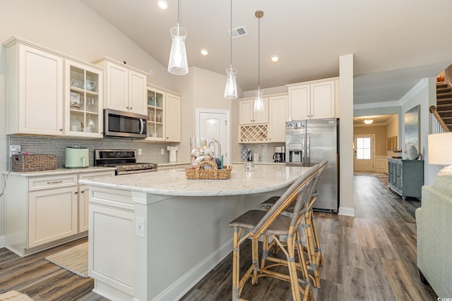 kitchen with appliances with stainless steel finishes, backsplash, pendant lighting, a center island with sink, and lofted ceiling