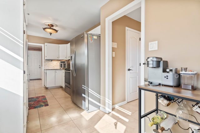 kitchen featuring light tile patterned floors, stainless steel fridge with ice dispenser, backsplash, stove, and white cabinets