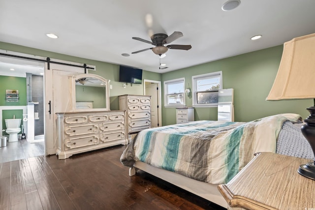 bedroom featuring ceiling fan, a barn door, dark hardwood / wood-style flooring, and ensuite bathroom