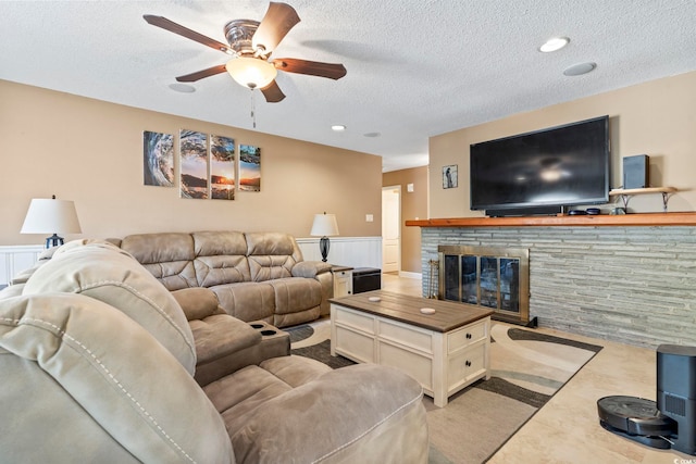 living room with a stone fireplace, ceiling fan, and a textured ceiling