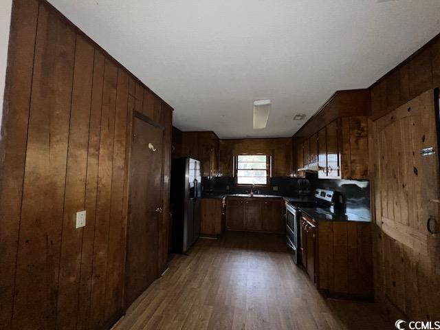 kitchen with dark hardwood / wood-style flooring, sink, stainless steel electric range oven, fridge, and wood walls