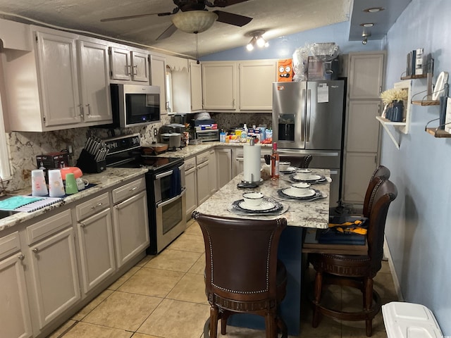 kitchen with ceiling fan, light stone countertops, decorative backsplash, light tile patterned floors, and appliances with stainless steel finishes