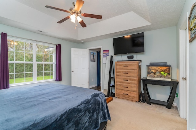 bedroom featuring light carpet, a textured ceiling, a tray ceiling, and ceiling fan