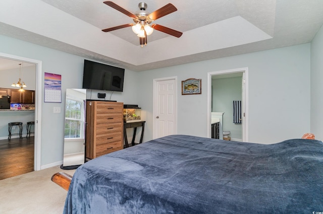 carpeted bedroom featuring ceiling fan with notable chandelier, a raised ceiling, fridge, and connected bathroom